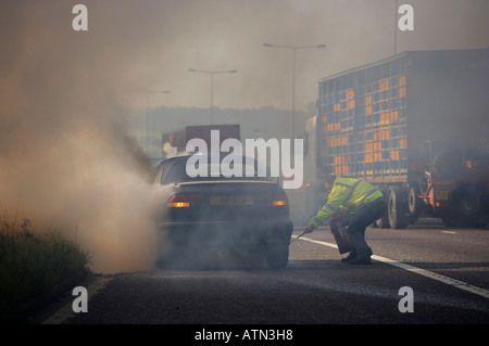 Les services d'urgence à l'aide d'EXTINCTEUR SUR LE VÉHICULE EN FEU SUR L'AUTOROUTE LA BANDE D'ARRÊT D'URGENCE Banque D'Images