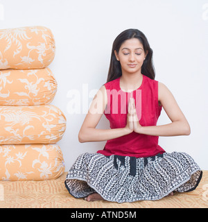 Jeune femme assise sur le lit dans une position de prière Banque D'Images