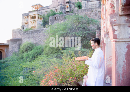 Portrait of a young man holding a plate de la poudre sur le balcon d'un fort, Neemrana Fort Palace, Alwar, au Rajasthan, Inde Banque D'Images