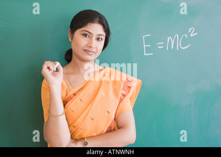 Portrait d'une enseignante avec une craie et debout devant un tableau noir Banque D'Images