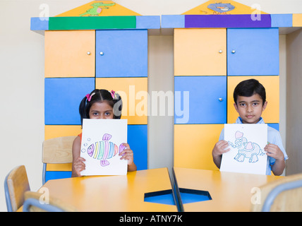Portrait d'un écolier et d'écolière montrant des peintures dans une salle de classe Banque D'Images