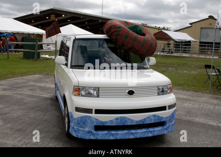 Petite voiture blanche portant un tam-o-shanter chapeau écossais à l'extérieur sur un jour nuageux Banque D'Images