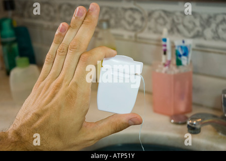 Detail shot of a hand holding a blank fil dentaire fort, avec lavabo dans l'arrière-plan flou. Banque D'Images