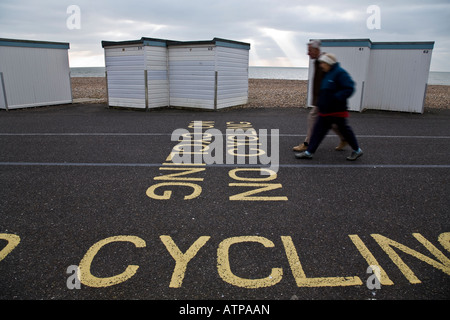 Couple en train de marcher le long de la voie à côté d'une rangée de cabines de plage sur le front de mer à Worthing, West Sussex, Angleterre. Banque D'Images