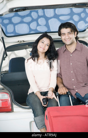 Portrait d'un jeune couple assis dans le coffre d'une voiture et souriant Banque D'Images