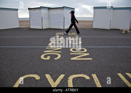 Femme promener son chien le long d'une allée à côté d'une rangée de cabines de plage sur le front de mer à Worthing, West Sussex, Angleterre. Banque D'Images