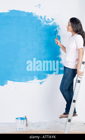 Portrait d'une jeune femme peindre un mur avec un rouleau à peindre et s'appuyant sur un escabeau Banque D'Images