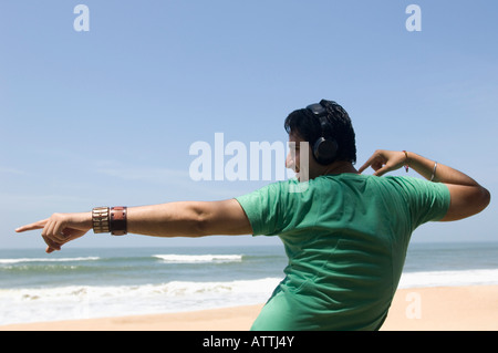Vue arrière d'un jeune homme portant des écouteurs et danser sur la plage Banque D'Images