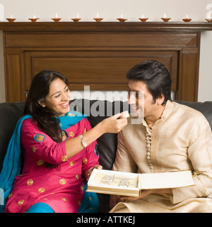 Close-up of a young woman feeding un morceau de burfi à a Mid adult man and smiling Banque D'Images