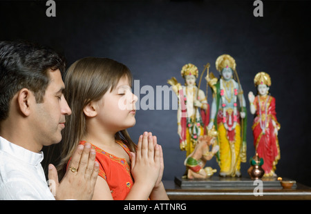 Mid adult man avec sa fille priant devant des statues de Dieu Banque D'Images