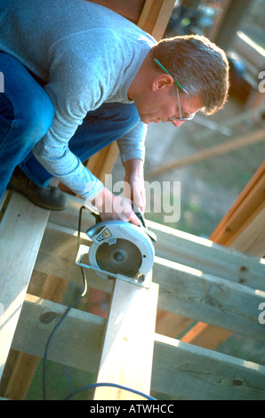 Carpenter l'âge de 58 ans à l'aide de scie de compétences pour aider à construire le pont de la cabine. Minnesota USA Nisswa Banque D'Images