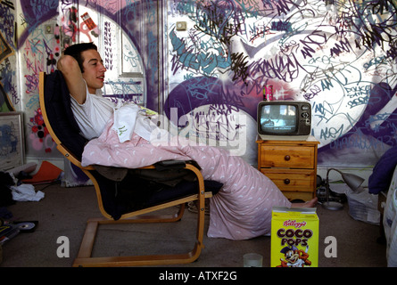 Adolescent assis sur une chaise enveloppée dans une couette à regarder la télévision dans sa chambre. Banque D'Images