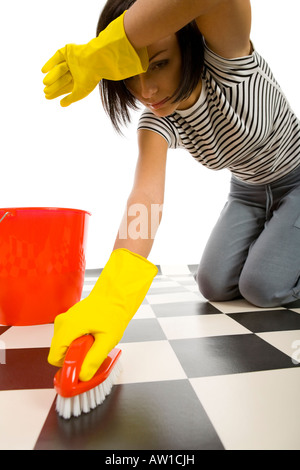 Jeune femme en jaune gants en caoutchouc à genoux et frotte le sol elle s est comme fatigué Vue de face fond blanc Banque D'Images