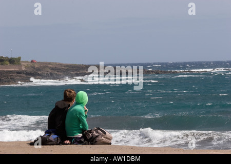 Jeune couple assis sur les rochers à la recherche à un très grosse mer El Medano Tenerife Banque D'Images