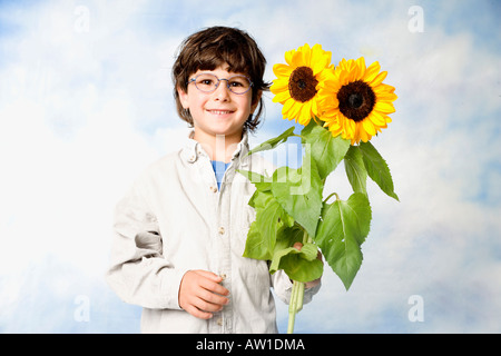 Young boy smiling en huis clos avec des tournesols à la main Banque D'Images