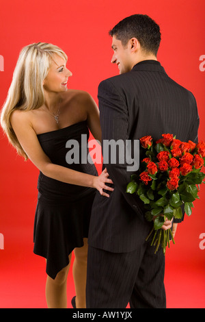 Jeune homme en costume se cache fleurs avant beautiful smiling woman l'homme est debout dos Banque D'Images