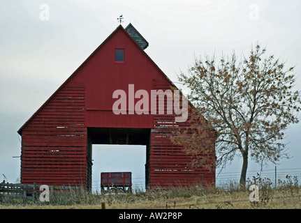 Le maïs rouge grange sur lit d'automne jour abritant un vieux wagon avec arbre à l'extérieur avec le cloud layden ciel au-dessus. Banque D'Images