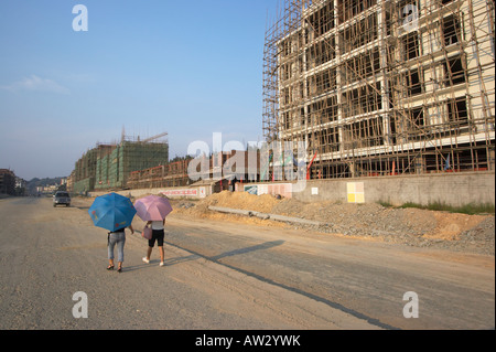 Les femmes marchant le long de la route à travers l'exécution du chantier, parasols, Guangxi, Chine Sanjiang Banque D'Images