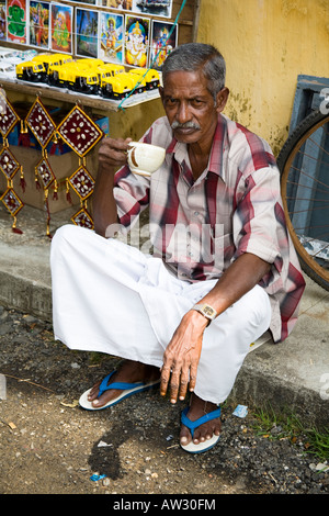 Propriétaire de boire du thé à l'extérieur d'une boutique, Mattancherry, Cochin, Kerala, Inde Banque D'Images