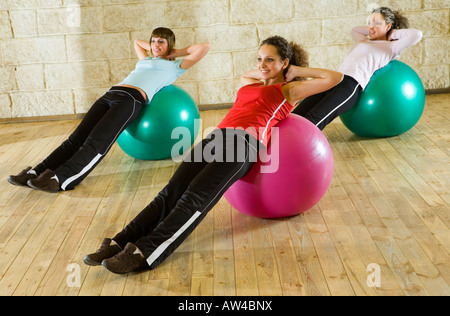 Un groupe de femmes faisant l'exercice couché sur big balls. Ils sont souriants et à quelque part. L'accent sur la femme en rouge shir. Banque D'Images
