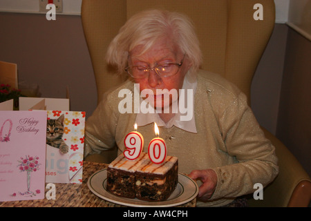 Dame âgée en soins infirmiers accueil célébrant son 90e anniversaire blowing out candles on cake sa Banque D'Images