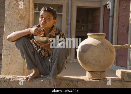 Portrait d'un jeune garçon en train de manger son petit-déjeuner sur un mur avec un pot en argile. Banque D'Images
