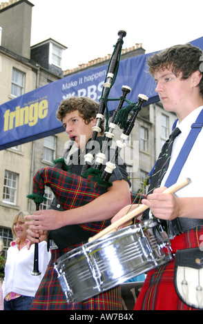 Deux jeunes hommes en costume national écossais jouant cornemuses et tambours en face de l'Edinburgh Fringe Festival banner Banque D'Images