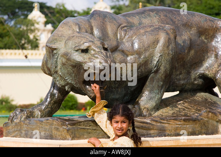 Petite fille indienne de toucher une statue en bronze d'un lion OU tigre de grincement dans les motifs de Mysore Palace Banque D'Images