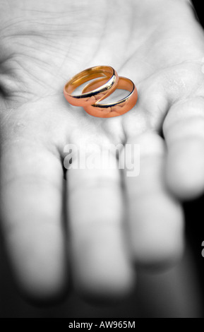 Un gros plan de deux bagues d'or dans une main en noir et blanc Banque D'Images