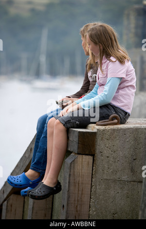 Deux adolescentes assis sur une jetée, donnant sur le port. Fowey. Cornwall. Banque D'Images