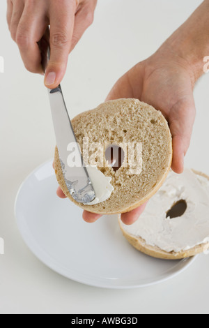 L'épandage à la main le fromage à la crème sur bagel Banque D'Images