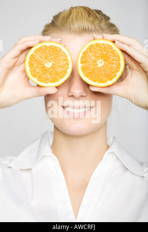 Femme blonde en riant tenant deux oranges en tranches devant ses yeux Banque D'Images