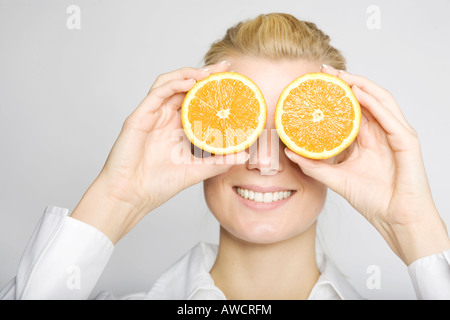 Femme blonde en riant tenant deux oranges en tranches devant ses yeux Banque D'Images