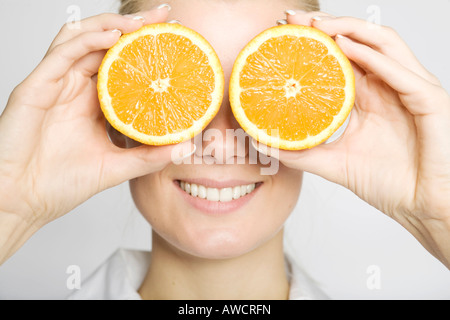 Femme blonde en riant tenant deux oranges en tranches devant ses yeux Banque D'Images