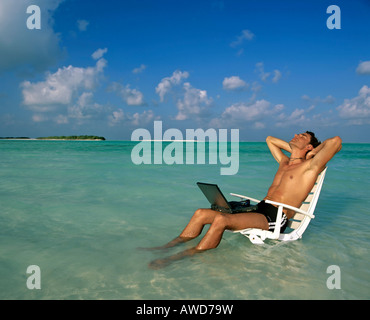 Jeune homme avec portable assis sur une chaise, travail et détente, vacances et stress, Maldives, océan Indien Banque D'Images