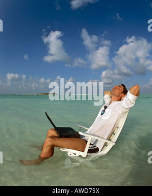 Jeune homme avec portable assis sur une chaise, travail et détente, vacances et stress, Maldives, océan Indien Banque D'Images