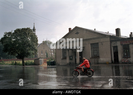 Teenager riding un cyclomoteur sur une route de campagne sous une pluie diluvienne, Kotulin, Pologne Banque D'Images