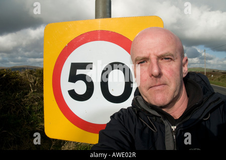 Homme debout par un 50 mile par heure vitesse limite signe de route sur l'âge de 50 ans avoir un mini mi crise de la vie Banque D'Images