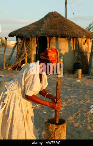 Vieille Femme battre le mil en face d'une hutte, ronde Sehitwa, Botswana, Africa Banque D'Images