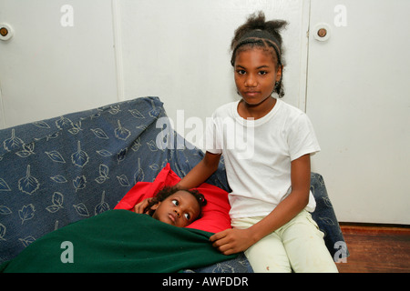 Jeune fille assise à côté d'une petite fille dans un lit de malade, de la vie quotidienne à un couvent des Ursulines et l'orphelinat à Georgetown, Guyana, au Sud Banque D'Images