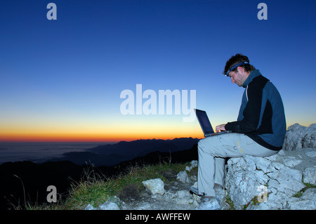 Homme avec portable au lever du soleil sur le sommet d'une montagne, montagne, piémont bavarois Breitenstein, Groupe Wendelstein, Haute-Bavière, Bava Banque D'Images