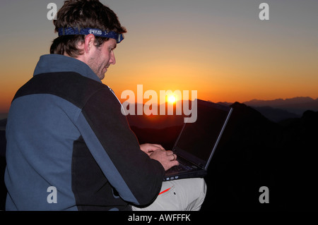 Homme avec portable au lever du soleil sur le sommet d'une montagne, montagne, piémont bavarois Breitenstein, Groupe Wendelstein, Haute-Bavière, Bava Banque D'Images