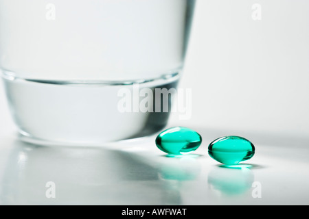 Deux comprimés d'ibuprofène verte à côté d'un verre d'eau. Banque D'Images