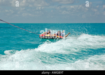 Close up horizontale d'un jeune couple aventureux équitation un donut gonflable 'tubing' dans la mer par une belle journée ensoleillée Banque D'Images