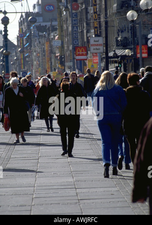 Foule marchant sur trottoir sur un jour froid, bâtiments en arrière-plan. Banque D'Images