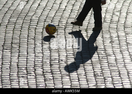 Joueur de football ombre sur la rue pavée Banque D'Images