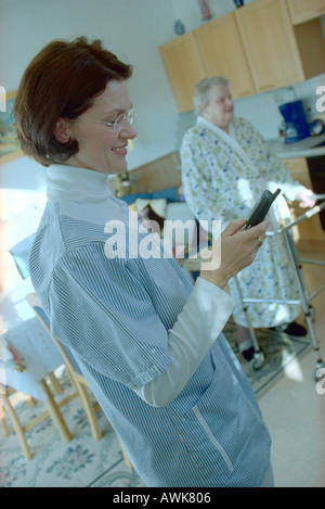 Profil de l'aide infirmière côté mobile phone with patient in background Banque D'Images