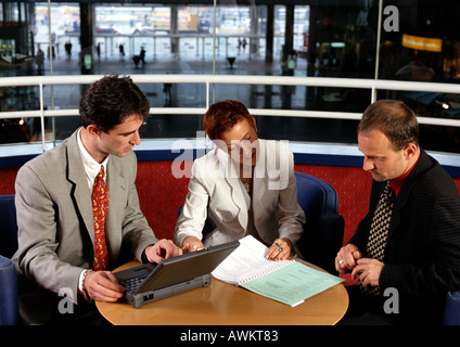 Trois personnes assis à table, un holding laptop computer Banque D'Images