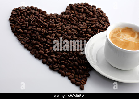 Café en grains en forme de cœur à côté d'une tasse de café Banque D'Images