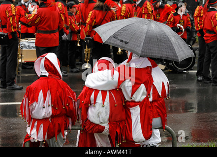 Adultes et deux enfants déguisés en arlequins, l'attente sous la pluie pour le début du Carnaval (Mardi Gras) défilé dans les cotisations Banque D'Images